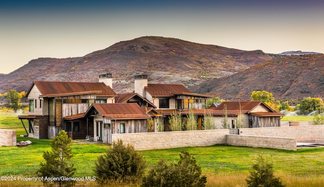 back house at dusk with a mountain view and a lawn