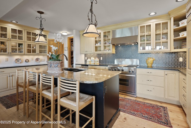 47 Mule Deer Run, Snowmass, CO 81654 - kitchen featuring wall chimney exhaust hood, high end stainless steel range oven, a kitchen island with sink, light wood-style flooring, and cream cabinets