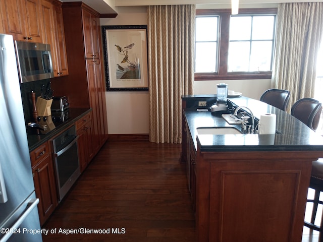 kitchen with appliances with stainless steel finishes, sink, dark wood-type flooring, and a breakfast bar