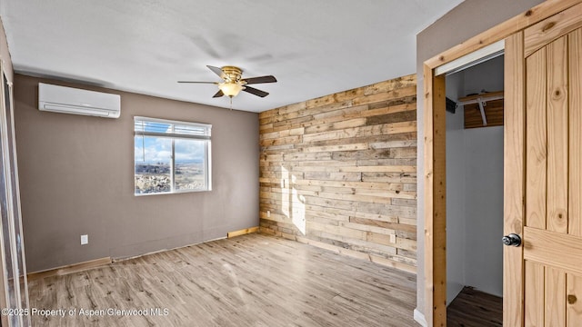 empty room featuring light wood-style floors, a wall mounted air conditioner, a ceiling fan, and wood walls