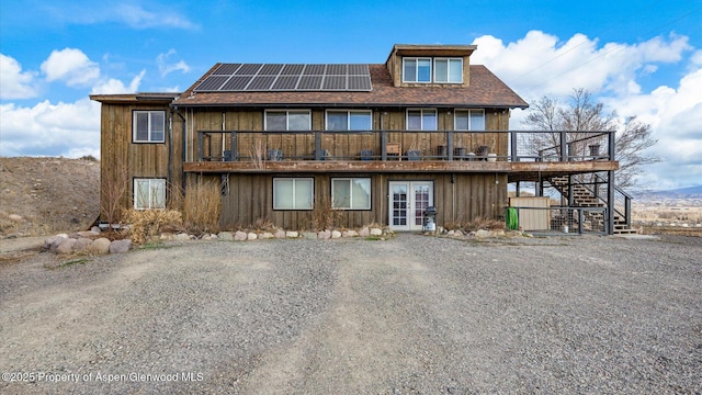 back of property featuring a wooden deck, roof with shingles, french doors, stairs, and roof mounted solar panels