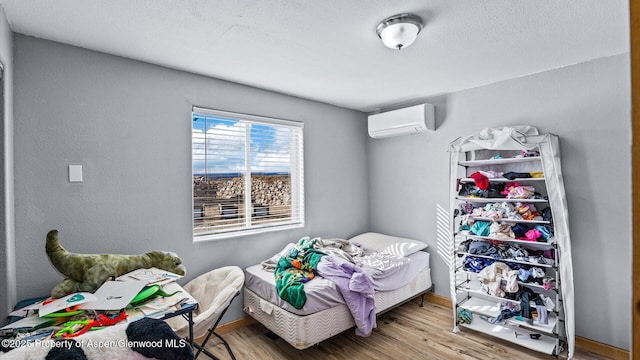 bedroom featuring baseboards, a wall mounted AC, and wood finished floors