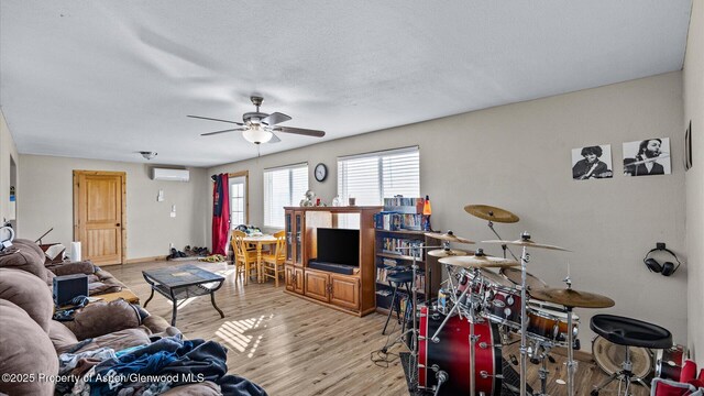 living area with an AC wall unit, a ceiling fan, and light wood-type flooring