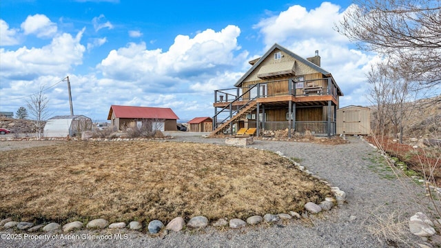 back of property with a chimney, a deck, stairway, an outdoor structure, and a shed