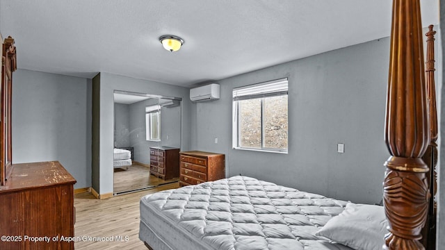 bedroom featuring a textured ceiling, a wall mounted AC, baseboards, a closet, and light wood-style flooring