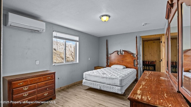bedroom featuring a textured ceiling, baseboards, a wall unit AC, and light wood-style flooring