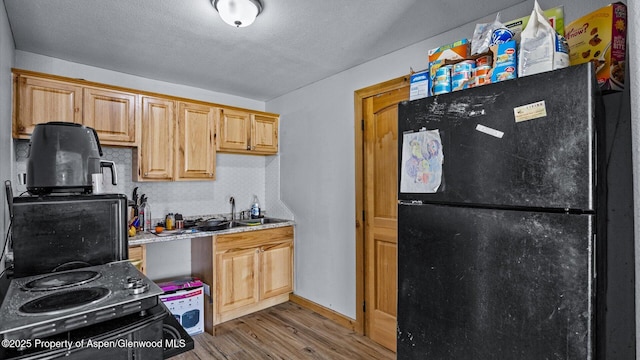 kitchen with wood finished floors, light countertops, baseboards, a sink, and black appliances