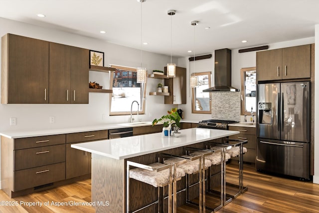 kitchen featuring appliances with stainless steel finishes, light countertops, wall chimney range hood, open shelves, and a sink