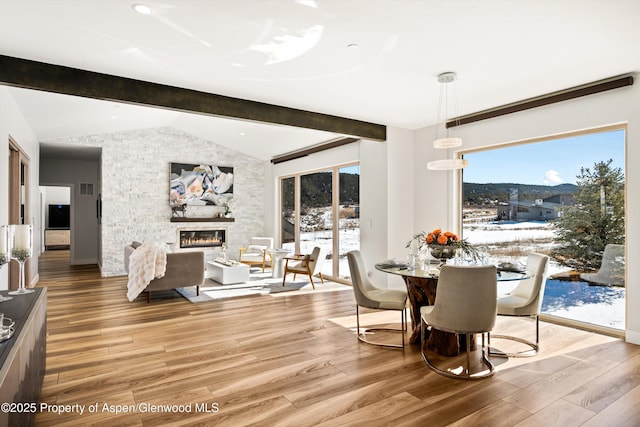 dining space featuring lofted ceiling with beams, a stone fireplace, wood finished floors, and visible vents