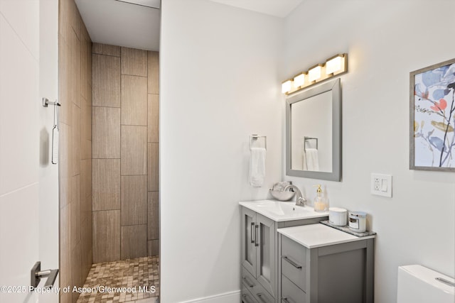 bathroom with a tile shower, vanity, and toilet