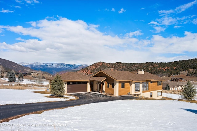 view of front of house with a garage, driveway, a chimney, and a mountain view