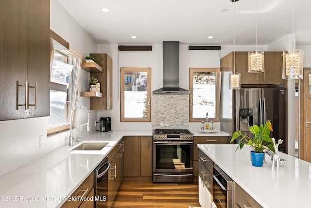 kitchen with appliances with stainless steel finishes, wood finished floors, light countertops, wall chimney range hood, and a sink