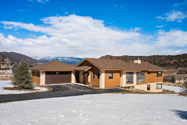 view of front facade with driveway, a chimney, an attached garage, and a mountain view