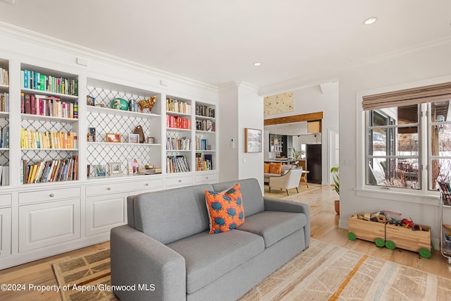 living area featuring built in shelves, light wood-type flooring, and ornamental molding