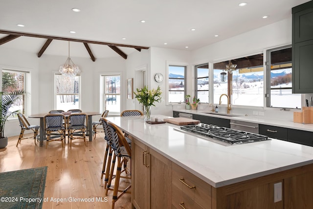 kitchen with light stone countertops, sink, light hardwood / wood-style flooring, stovetop, and hanging light fixtures