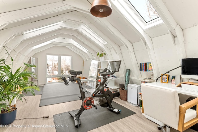 exercise room with vaulted ceiling with skylight and light wood-type flooring