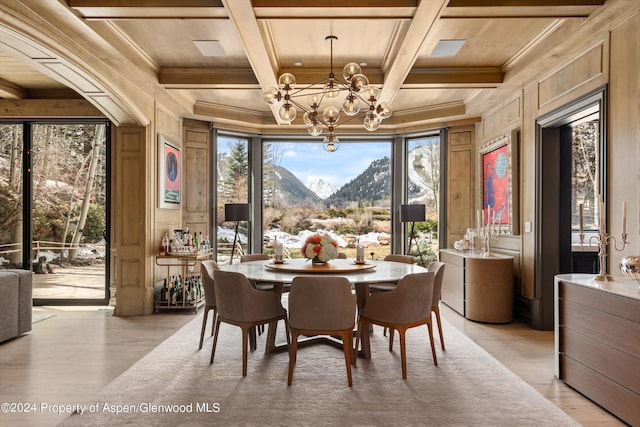 dining area with beamed ceiling, coffered ceiling, a notable chandelier, a mountain view, and light wood-type flooring