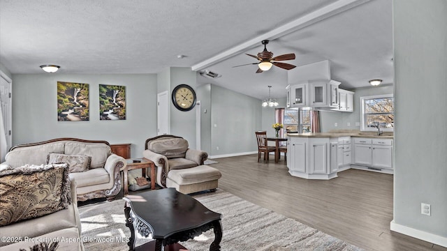 living room with ceiling fan with notable chandelier, vaulted ceiling with beams, baseboards, and wood finished floors