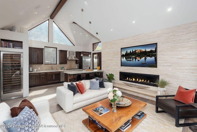 living area with beverage cooler, beam ceiling, a fireplace, light wood-style floors, and high vaulted ceiling