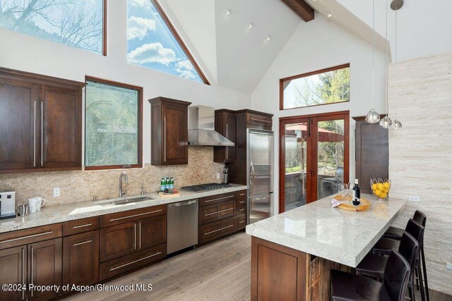 kitchen with beam ceiling, a sink, stainless steel appliances, french doors, and wall chimney range hood