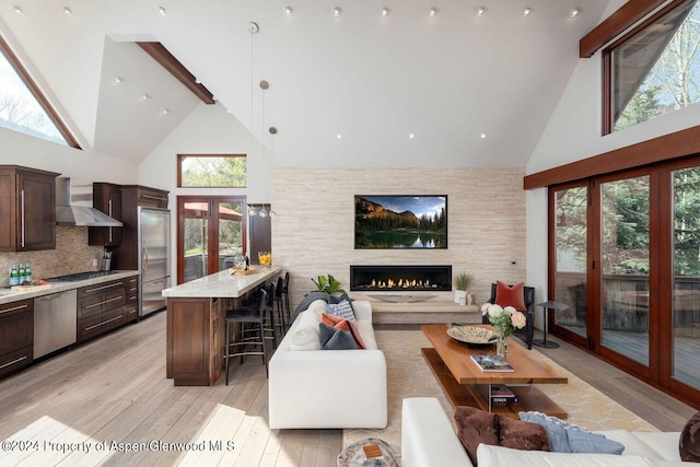 living room featuring high vaulted ceiling, light wood-style flooring, french doors, beamed ceiling, and a large fireplace