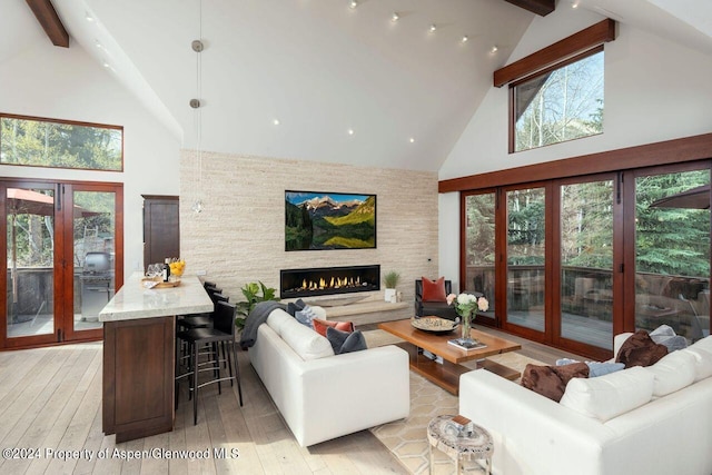 living room with a stone fireplace, beam ceiling, and light wood-type flooring