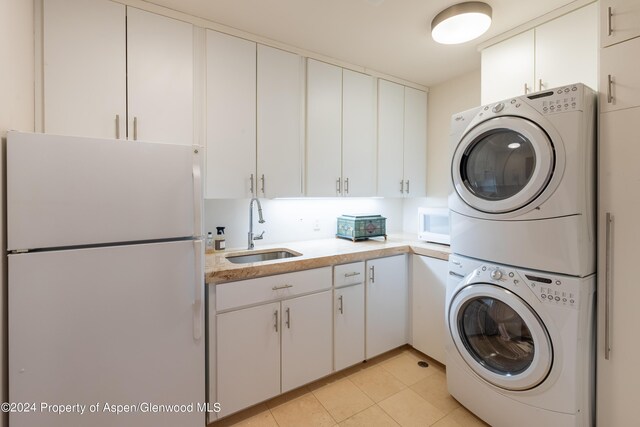 laundry area featuring stacked washing maching and dryer, light tile patterned flooring, cabinet space, and a sink