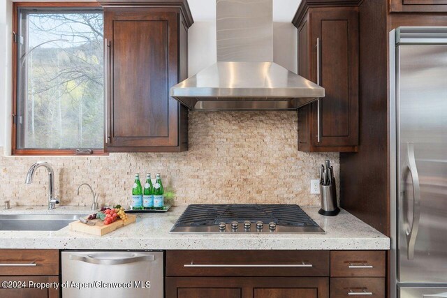 kitchen with a sink, appliances with stainless steel finishes, wall chimney range hood, decorative backsplash, and dark brown cabinets