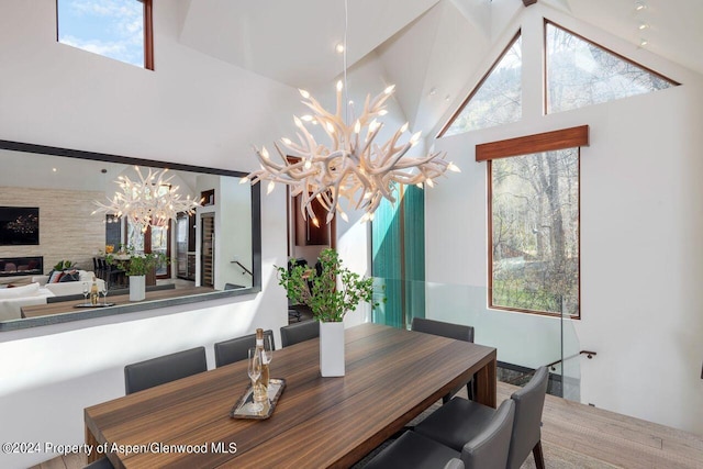 dining room with a wealth of natural light, a notable chandelier, high vaulted ceiling, and a large fireplace