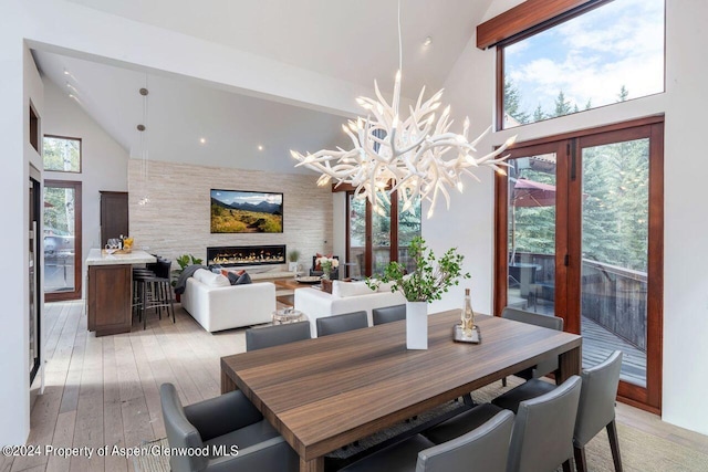 dining space featuring high vaulted ceiling, a large fireplace, light wood-style floors, and an accent wall