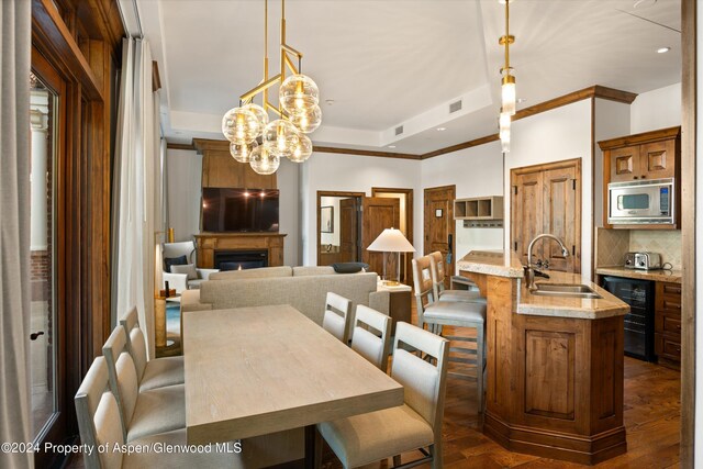 dining room with dark hardwood / wood-style flooring, ornamental molding, sink, an inviting chandelier, and wine cooler