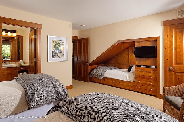 bedroom with light colored carpet, ensuite bath, and sink