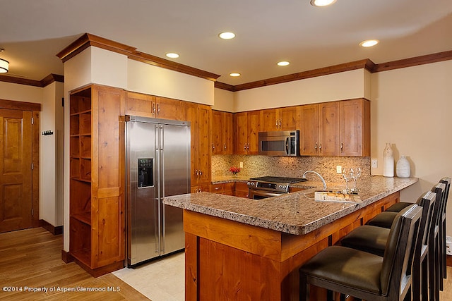 kitchen with a breakfast bar, decorative backsplash, ornamental molding, appliances with stainless steel finishes, and kitchen peninsula