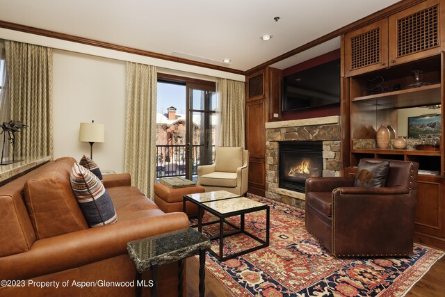 living room with hardwood / wood-style floors, a stone fireplace, and crown molding