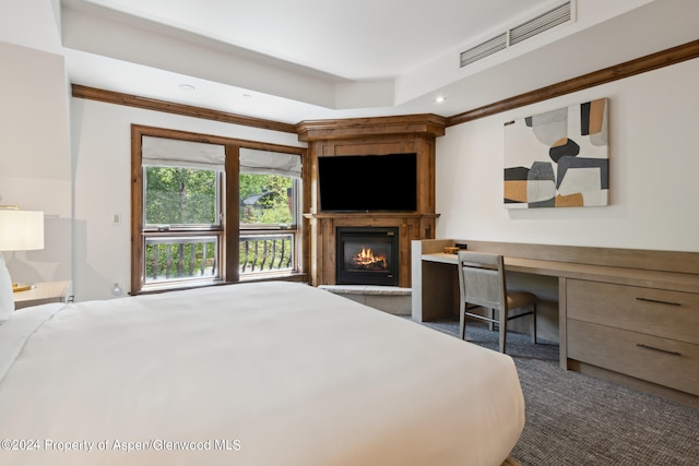 bedroom featuring a tray ceiling, built in desk, dark colored carpet, and a large fireplace