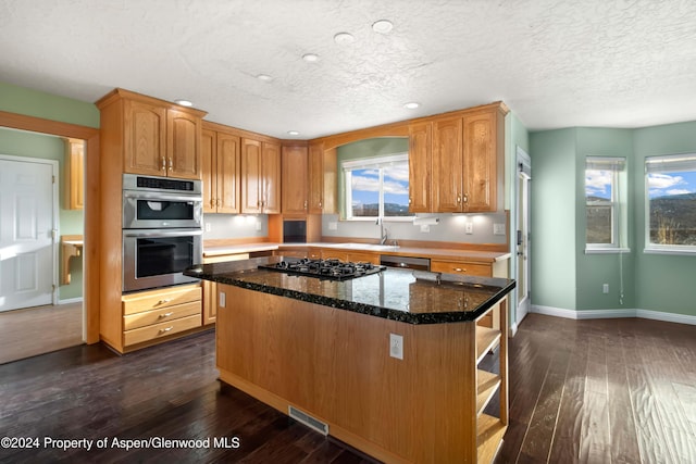 kitchen featuring a kitchen island, dark wood-type flooring, appliances with stainless steel finishes, and dark stone counters