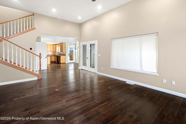 unfurnished living room with a towering ceiling, french doors, and dark hardwood / wood-style flooring