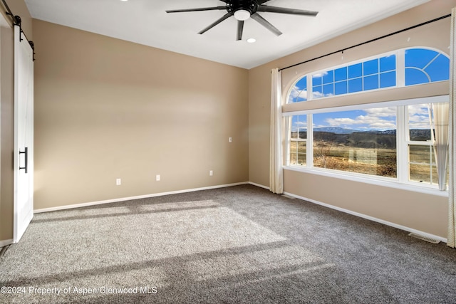 carpeted empty room featuring ceiling fan and a barn door