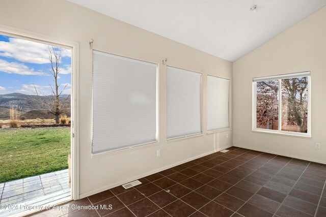 unfurnished room featuring a mountain view, dark tile patterned floors, and vaulted ceiling