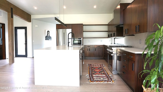 kitchen with premium appliances, sink, dark brown cabinets, and an island with sink