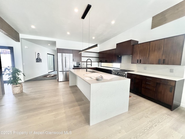 kitchen featuring sink, appliances with stainless steel finishes, a kitchen island with sink, pendant lighting, and light hardwood / wood-style floors