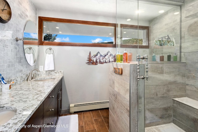 full bath with a baseboard heating unit, a tile shower, a sink, and wood finished floors