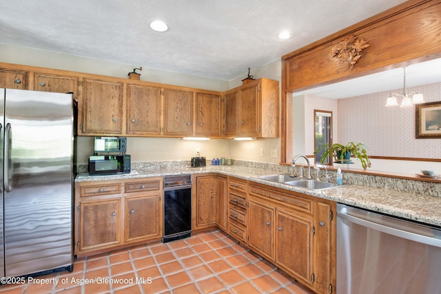 kitchen featuring wallpapered walls, stainless steel appliances, brown cabinets, a sink, and a notable chandelier