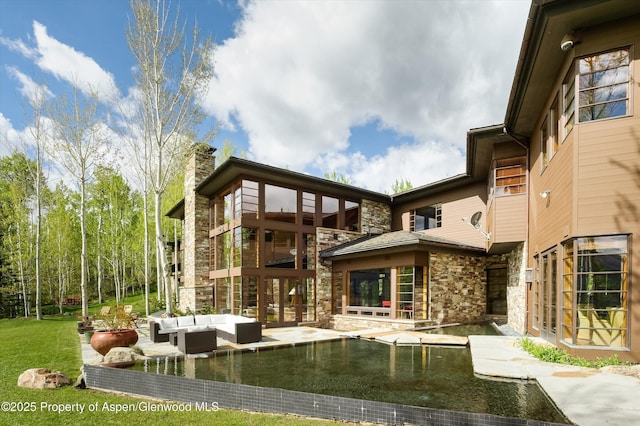 rear view of house featuring a chimney, an outdoor hangout area, a patio area, and stone siding