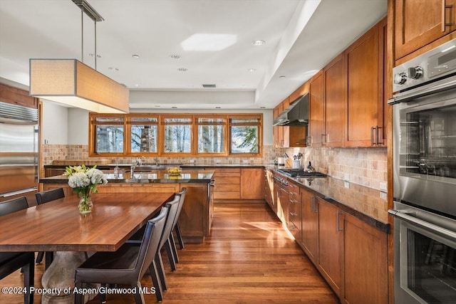 kitchen featuring butcher block counters, pendant lighting, appliances with stainless steel finishes, exhaust hood, and light wood-type flooring