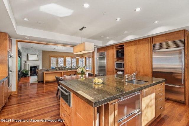 kitchen with stainless steel built in refrigerator, sink, decorative light fixtures, and an island with sink