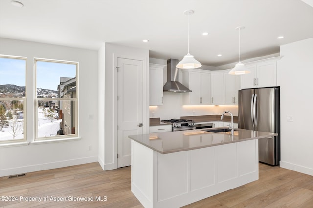 kitchen with white cabinets, sink, wall chimney exhaust hood, an island with sink, and stainless steel appliances