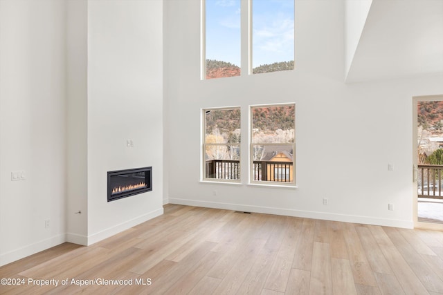 unfurnished living room featuring a towering ceiling and light hardwood / wood-style flooring