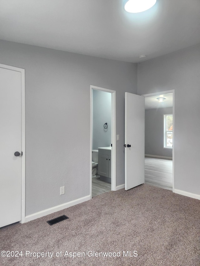 unfurnished bedroom with ensuite bathroom and light colored carpet