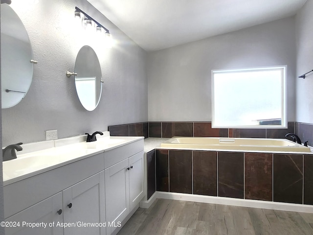 bathroom featuring tiled tub, vanity, and wood-type flooring